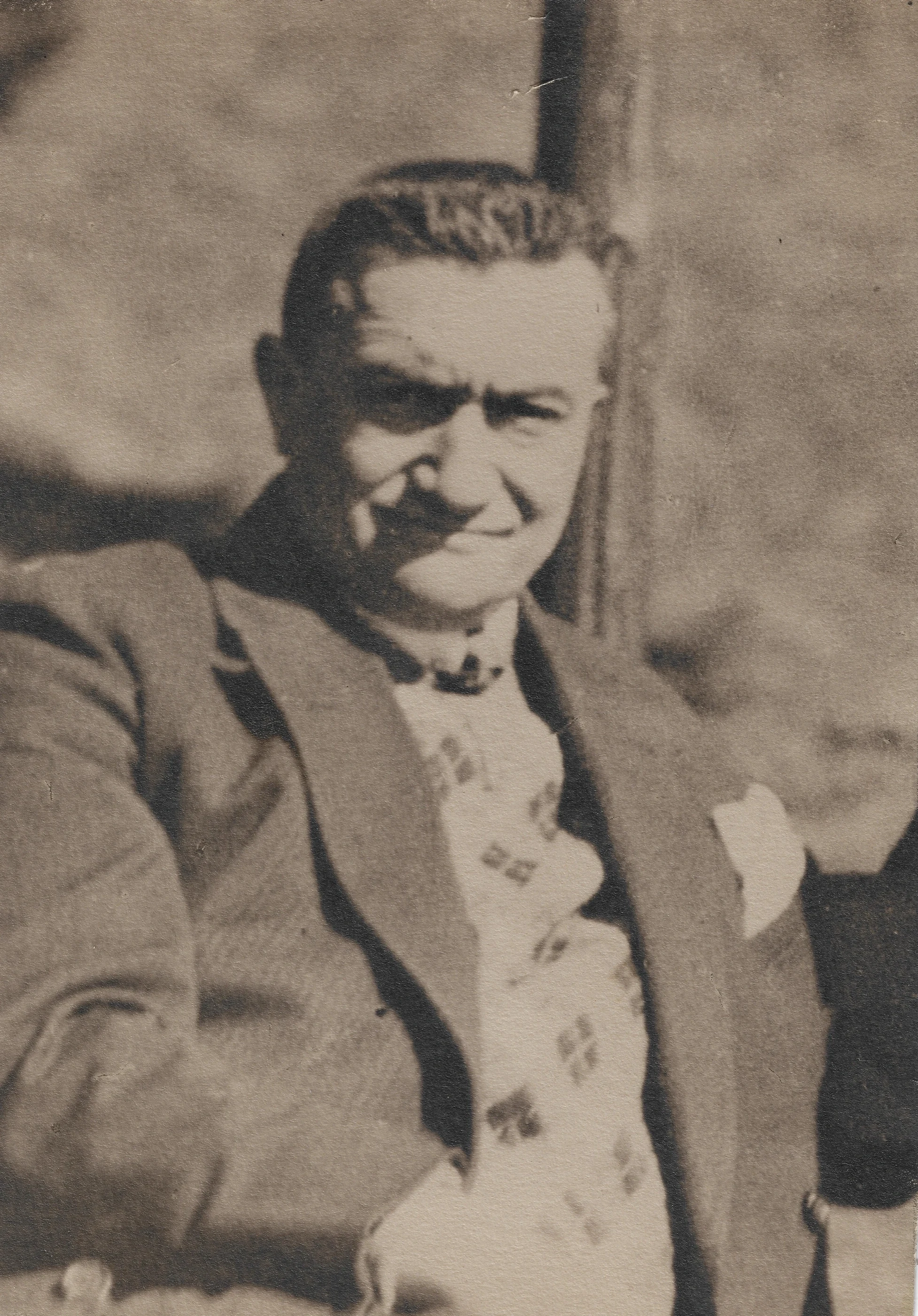 Late-life portrait of Paul Reichenbach seated outdoors in a jacket, patterned sweater and tie